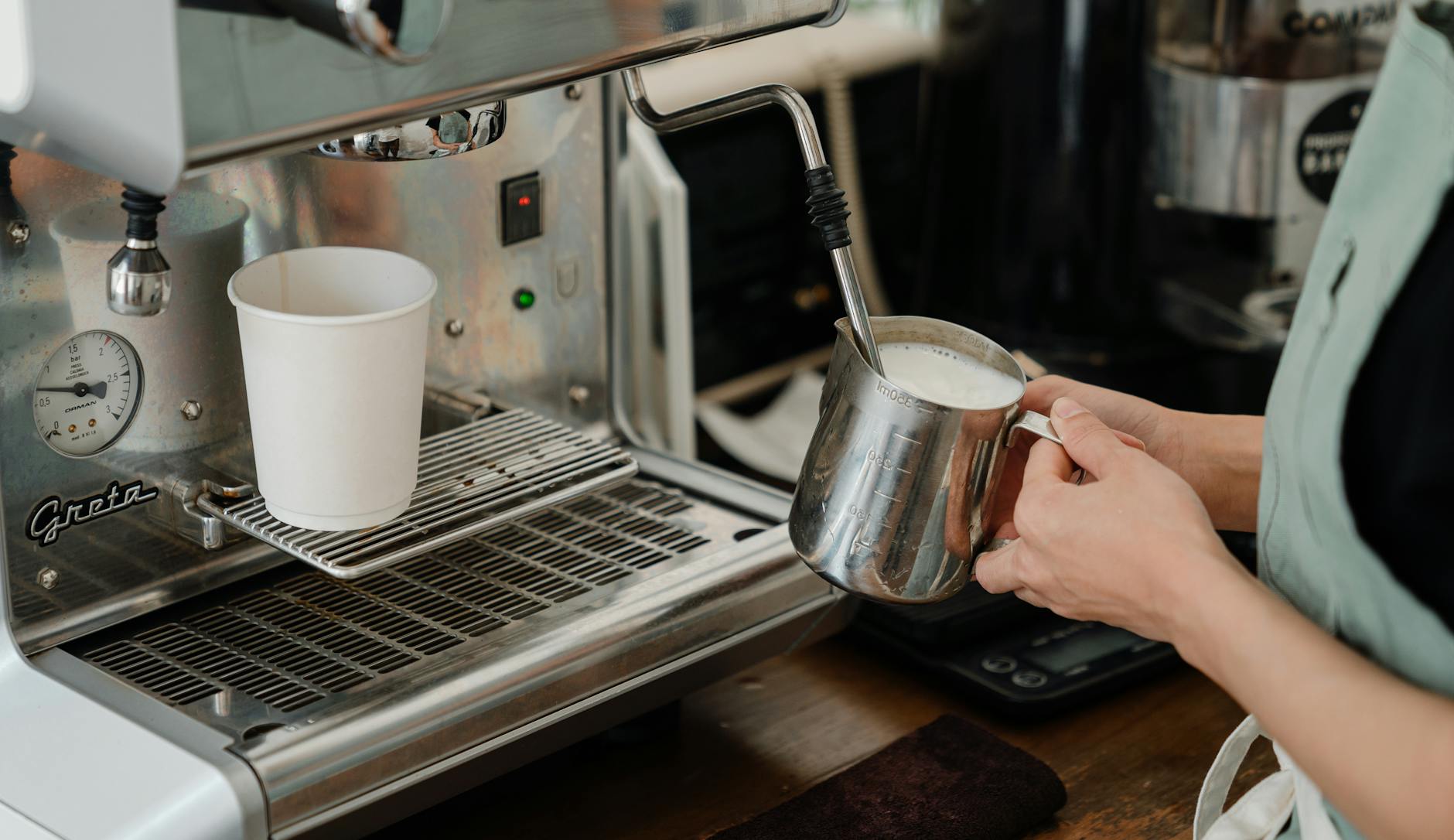 Barista spienia mleko dyszą pary ekspresu w nowoczesnej kawiarni
